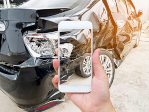 A Person Taking a Photograph of a Damaged Front of a Car